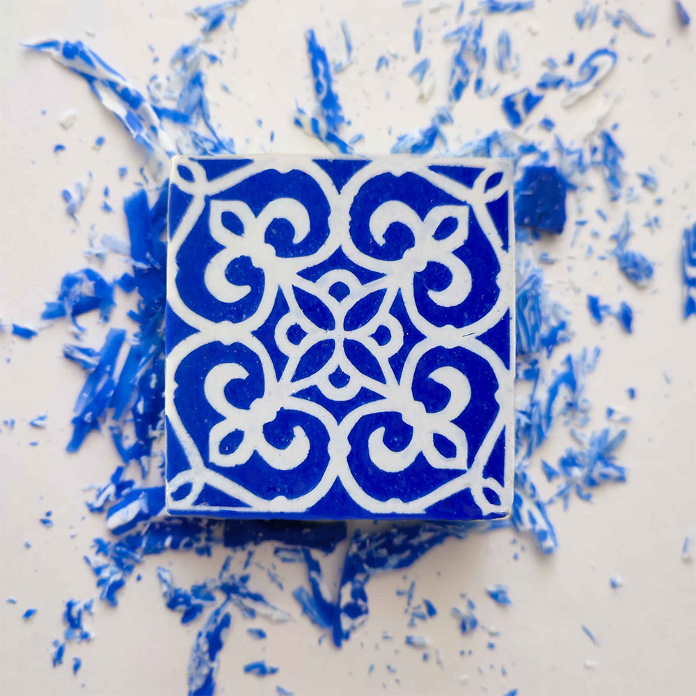 The Amêndoa Royale Tile Soap Bar by Lisbão features a square blue design with white geometric and floral patterns, displayed on a white background with blue shavings.