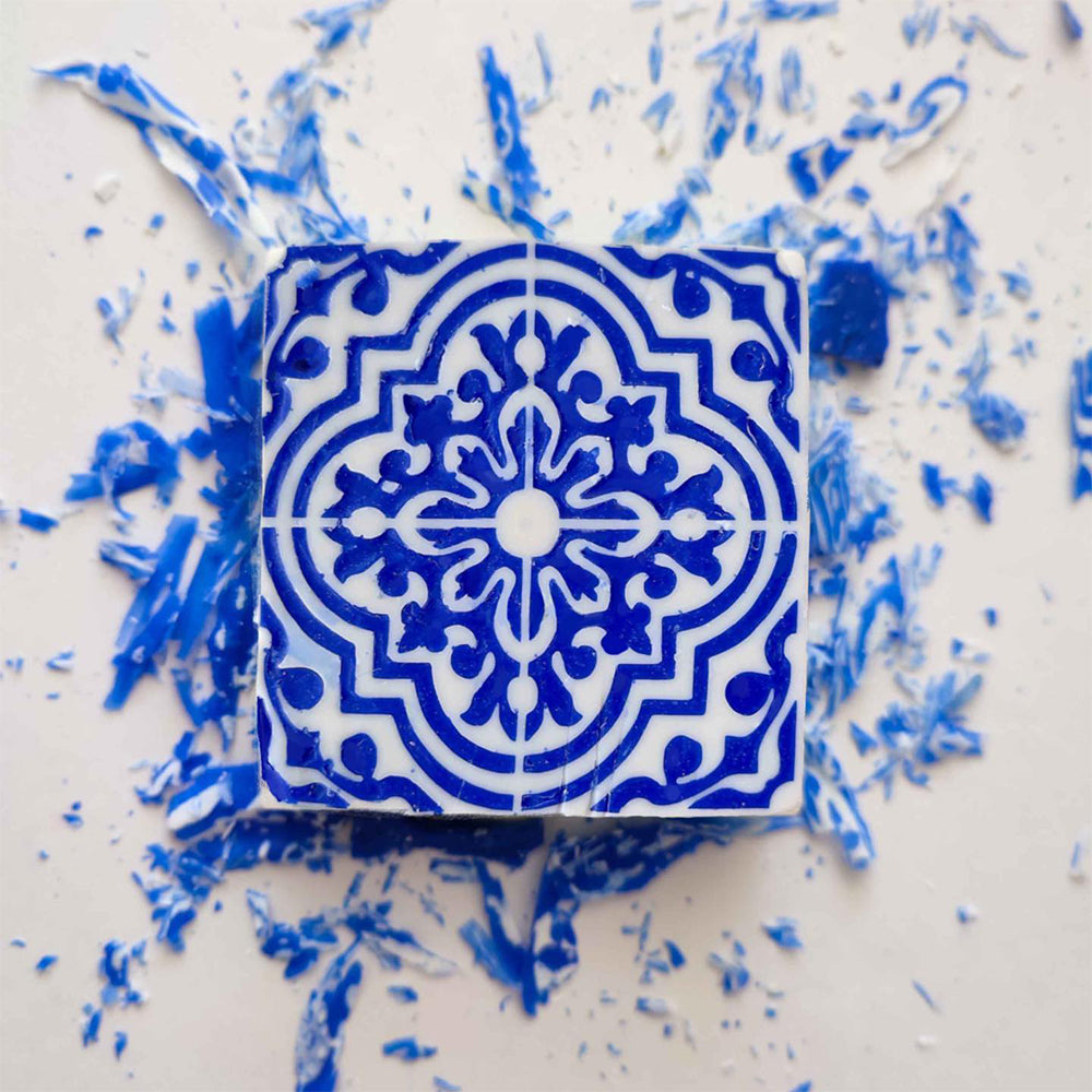 The Amêndoa Royale Tile Soap Bar by Lisbão displays a blue and white geometric Portuguese tile design, set on a light surface with scattered blue and white soap shavings.