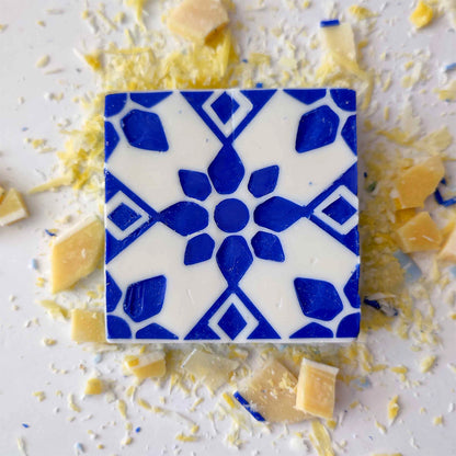 Pastel de Azulejo by Lisbão features a square soap with a blue geometric floral pattern on white, accented by yellow and beige shards—handmade and inspired by classic Portuguese azulejo tile designs for a unique touch.