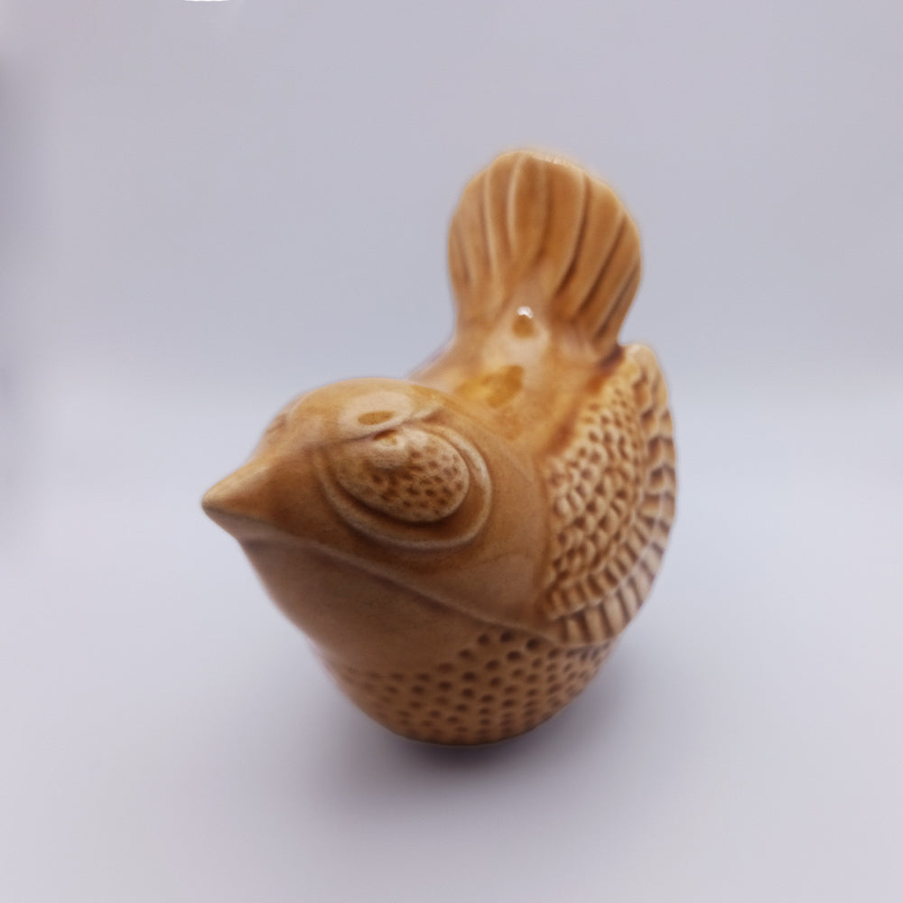 A close-up image of the Ceramic Bird Figurine by Tejo Shop. This small, glossy brown ceramic piece is handmade with detailed features like textured wings and feathers, combined with shiny, smooth surfaces. Positioned against a plain light background, it’s perfect for elegant home decor.