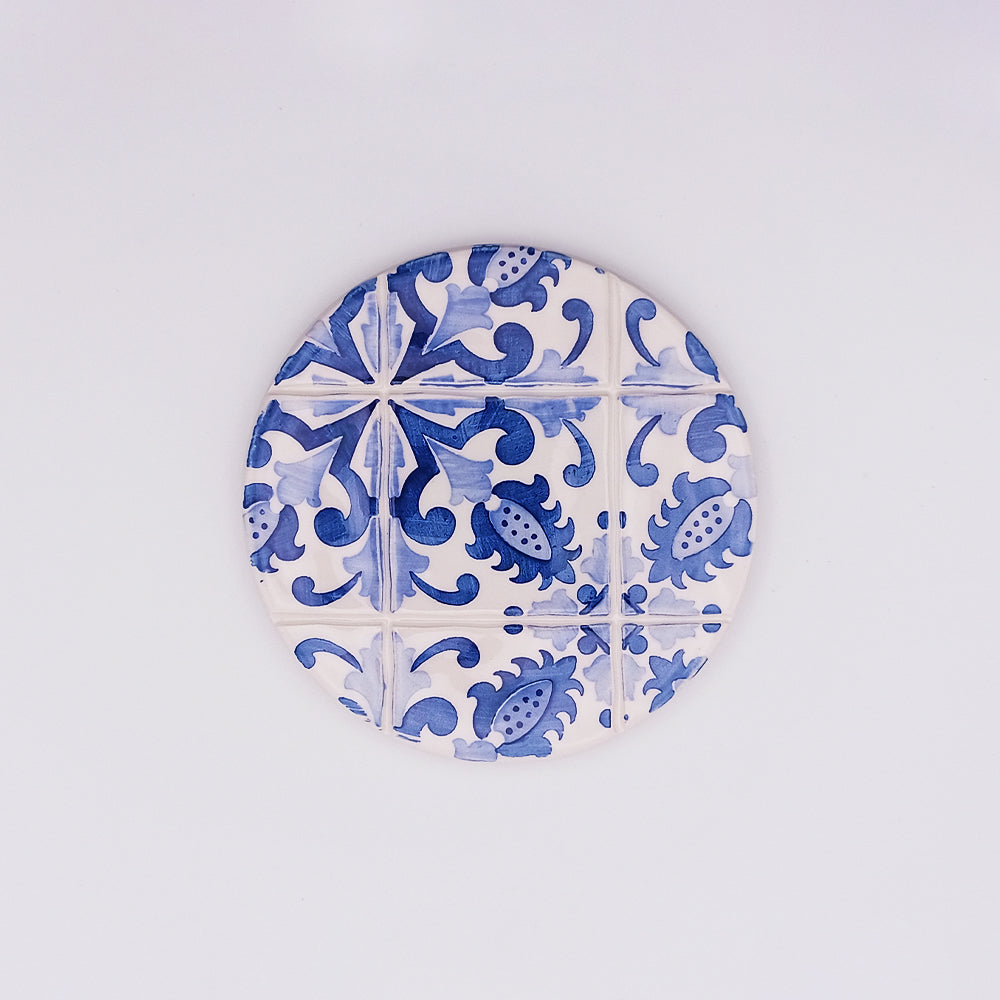 A **Lagos Ceramic Cup Pad** by **Tejo Shop**, featuring a blue and white pattern with intricate floral and geometric designs. This hand-painted cup pad has a vintage, tile-like appearance, elevating your dining experience against a plain white background.