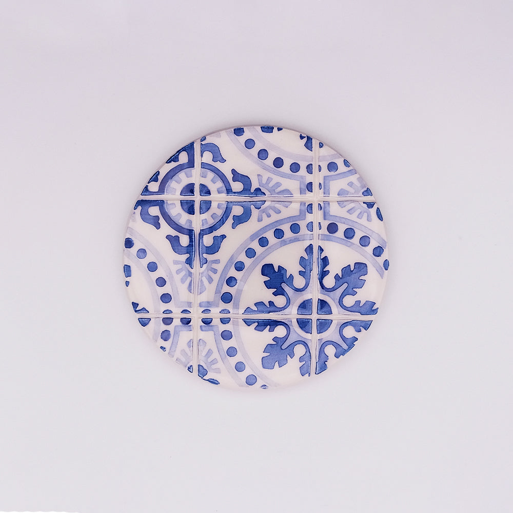 A round Liberdade Ceramic Cup Pad with a blue and white intricate pattern resembling traditional Portuguese tiles, featuring swirling lines and floral motifs, perfect for holding your coffee or tea. Photographed against a plain white background by Tejo Shop.