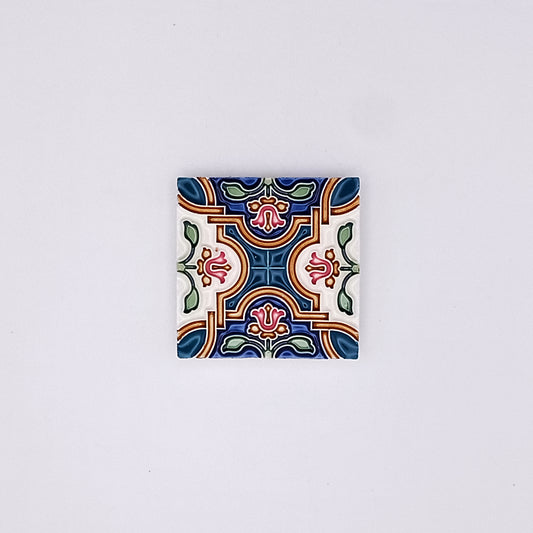 A small square Traditional Ceramic Small Tile with a colorful, symmetrical floral pattern on a white background. The design features blue, green, red, and yellow accents, embodying Portuguese sophistication from Tejo Shop.