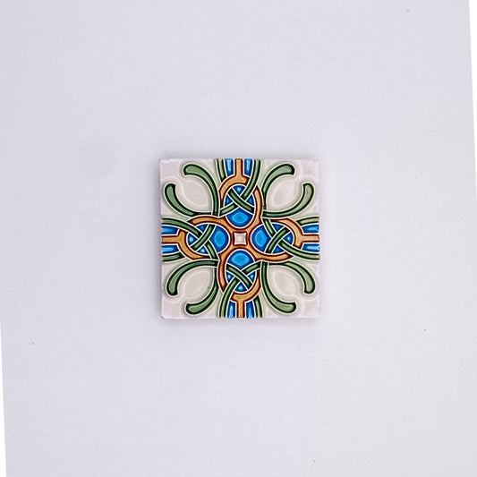 A square Small Mediterranean Tile from Tejo Shop with a symmetrical, colorful abstract design featuring interlocking shapes in blue, green, and orange on a white background.