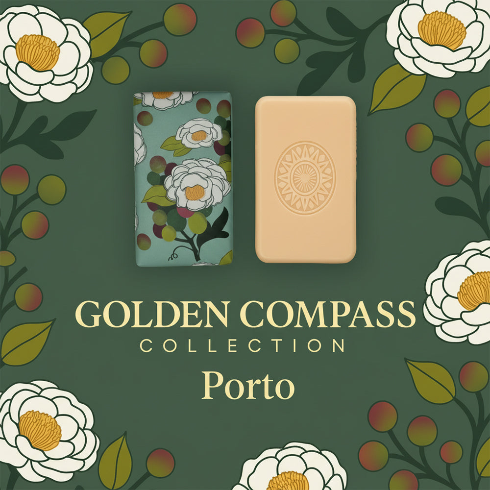 Two rectangular Porto 1394 – Birthplace of the Navigators soap bars by 100ml—one with a floral pattern, one plain beige embossed with a compass—are set on green with white flowers and red berries. Text: “GOLDEN COMPASS COLLECTION Porto.”.