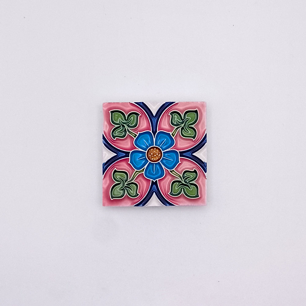 Decorative Spanish Tiles from Tejo Shop featuring a colorful floral design with blue, pink, and green petals, centered around a small orange dot, against a grey background, adding an artistic flair.