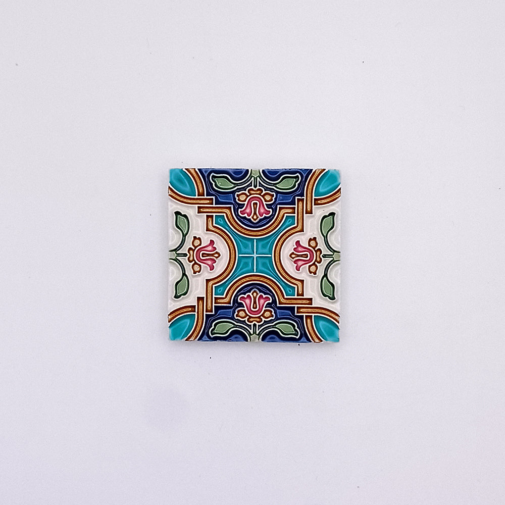 A square Tejo Shop Spanish Small Tile with a colorful, intricate symmetrical pattern, featuring bold shapes and colors such as teal, red, yellow, and green on a white background.