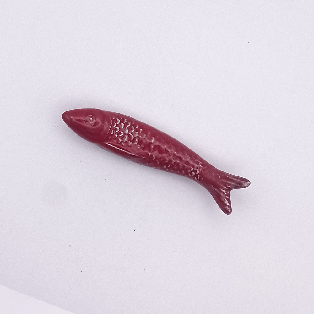 The Ceramic Sardine Fridge Magnet by Tejo Shop is a small, intricately detailed fish-shaped object made of maroon-colored ceramic. This charming piece of kitchen decor features precisely crafted scales, fins, and an open mouth. Displayed against a plain white background, it serves as a delicate Portuguese icon.