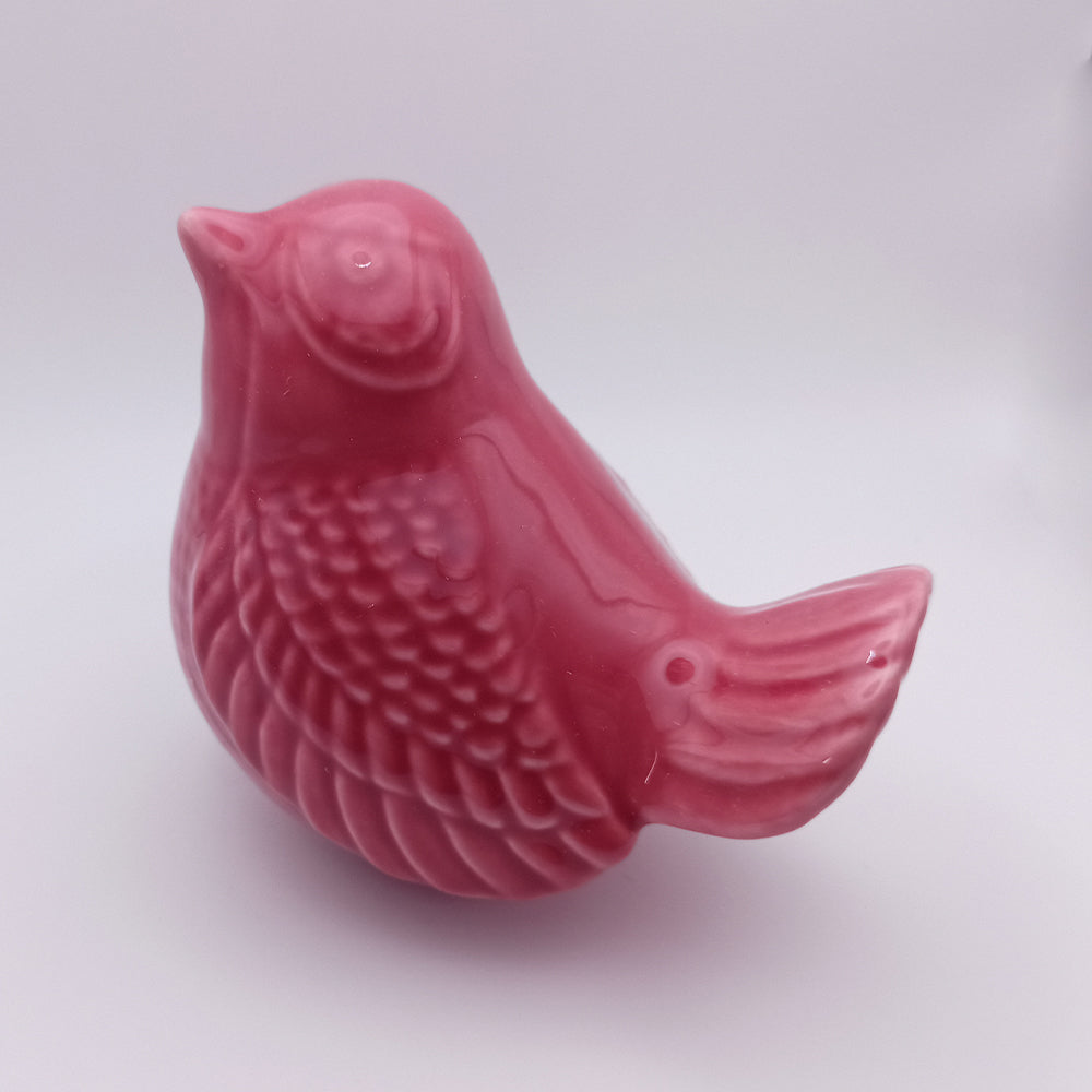 A small, pink Ceramic Bird looking up Figurine from Tejo Shop stands against a plain white background. This handmade piece features intricate feather details on its side and tail, a smooth, glossy finish, and a simplistic, rounded design—making it perfect for home decor.