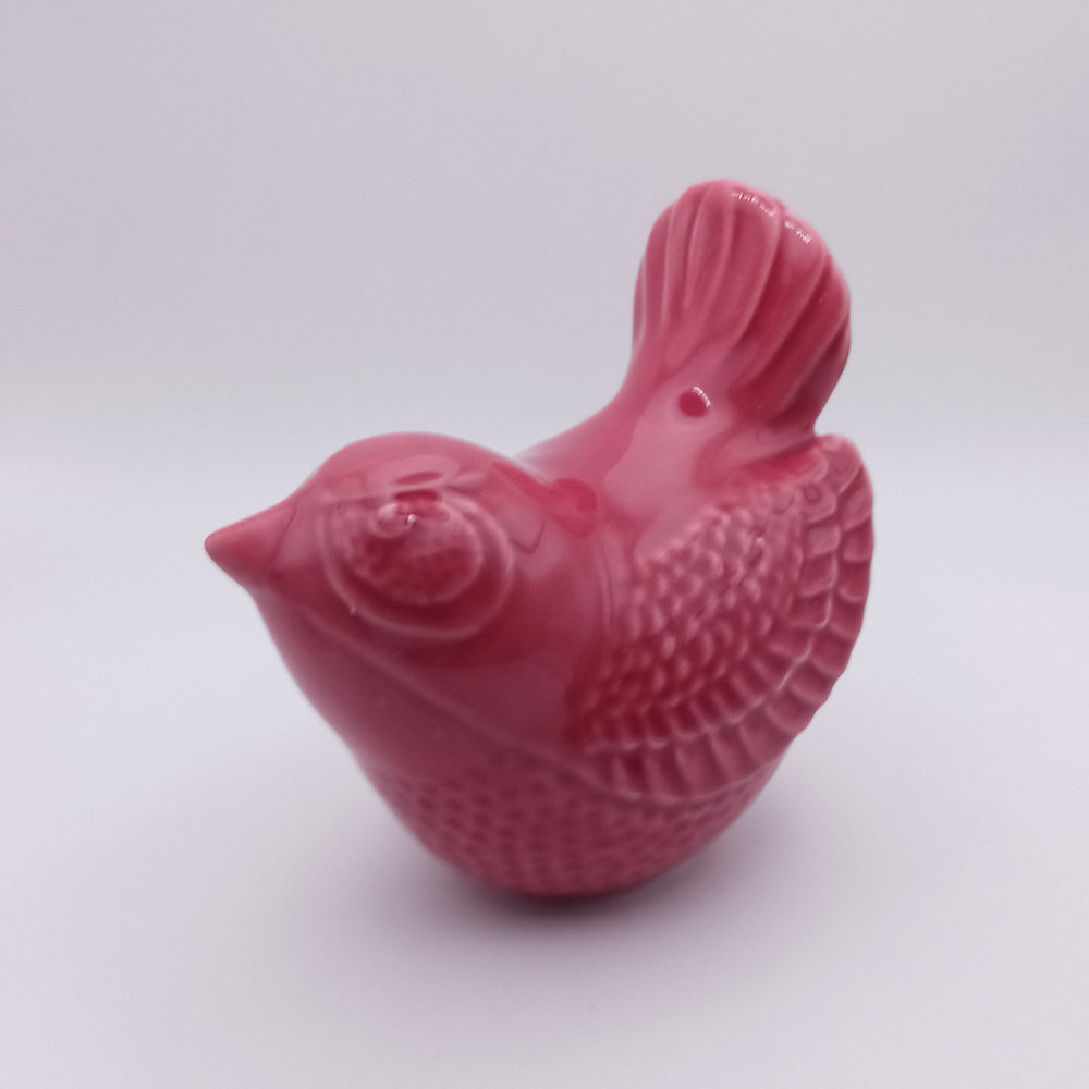 The Tejo Shop Ceramic Bird Figurine is a small, glossy ceramic piece in a vibrant pink color. It features detailed feather patterns on its body, wings, and tail. This handmade figurine is captured in profile view, facing left against a plain white background—ideal for home decor.