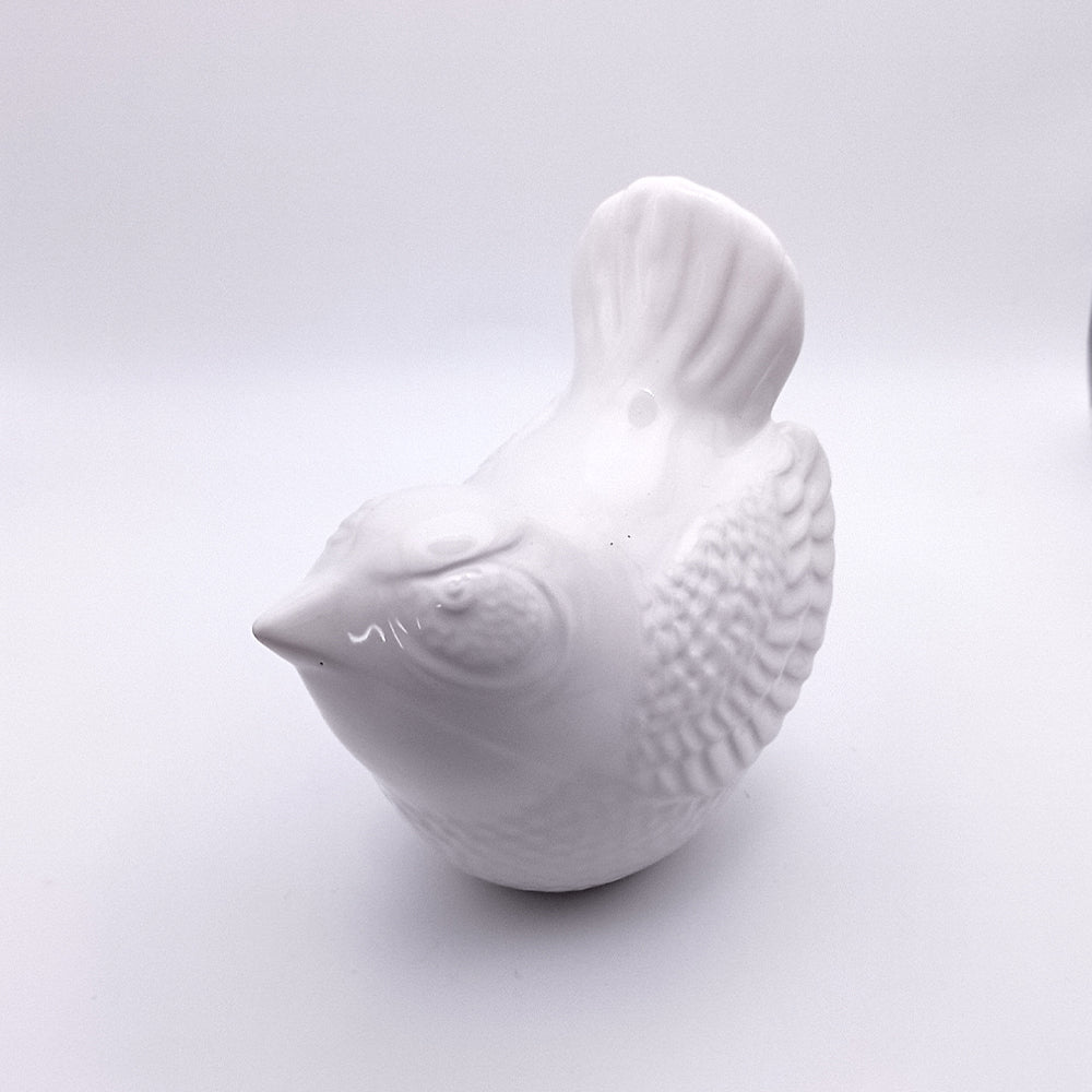 A photo of the Ceramic Bird Figurine by Tejo Shop, featuring a small handmade ceramic bird with detailed feathers and a round body. The figurine is shown from a slight angle, highlighting its textured surface and simplistic design, making it an ideal piece for home decor. The background is plain and white.